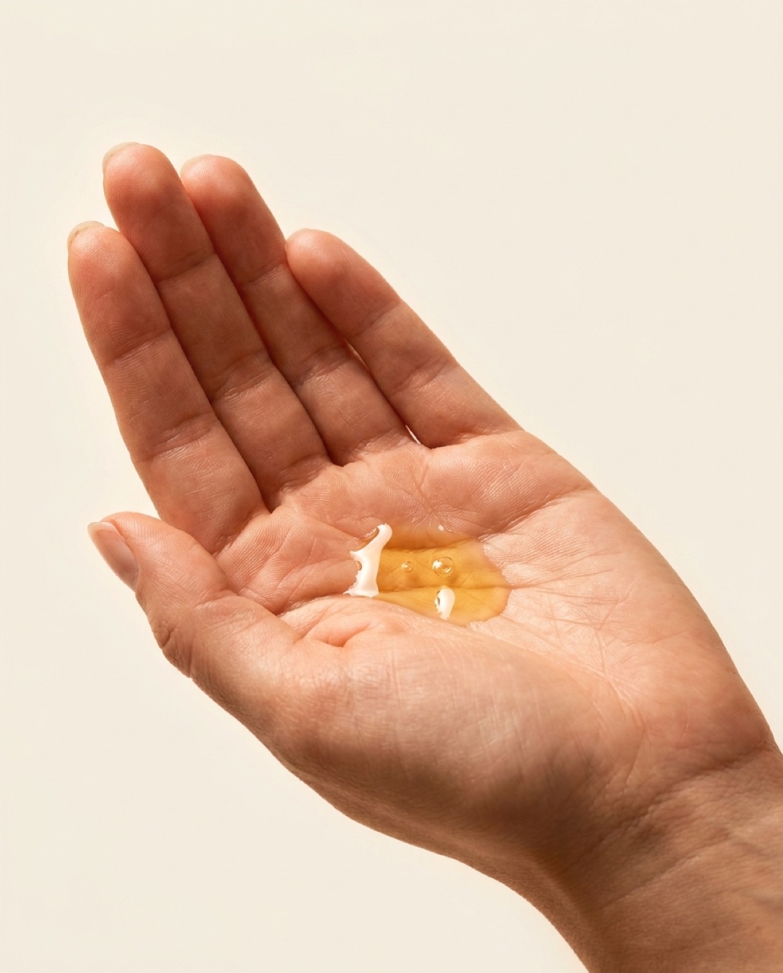 An open palm with golden drops of the face oil pooled at its centre.
