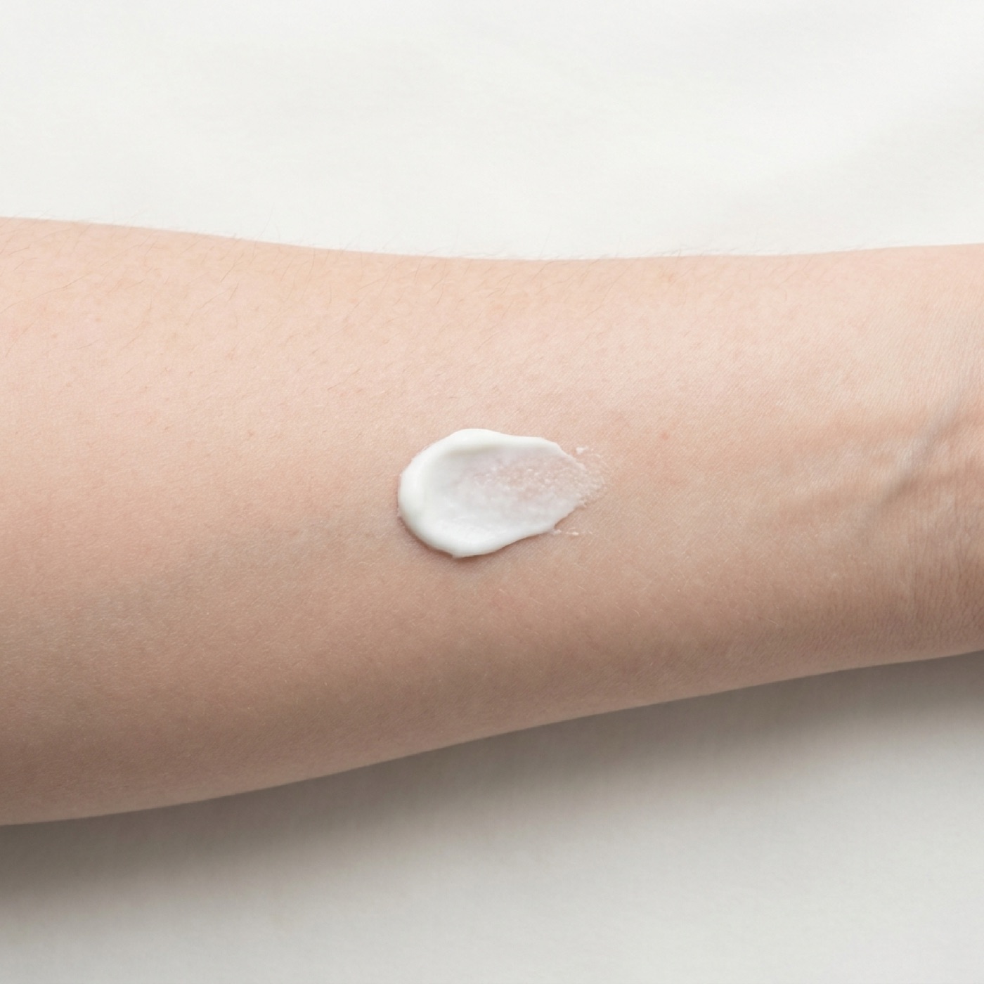 A swatch of white cream half rubbed into fair inner-forearm skin, showing the finish.