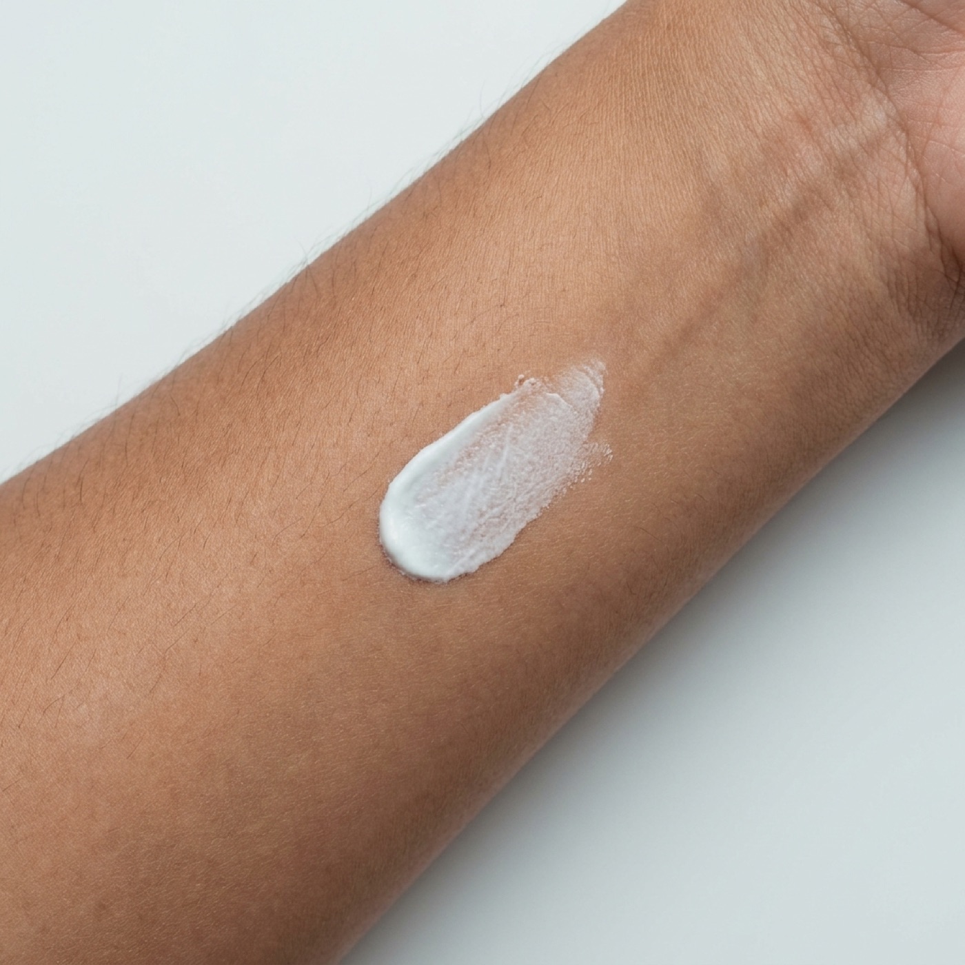 A swatch of white cream half rubbed into medium-tan inner-forearm skin, showing the finish.