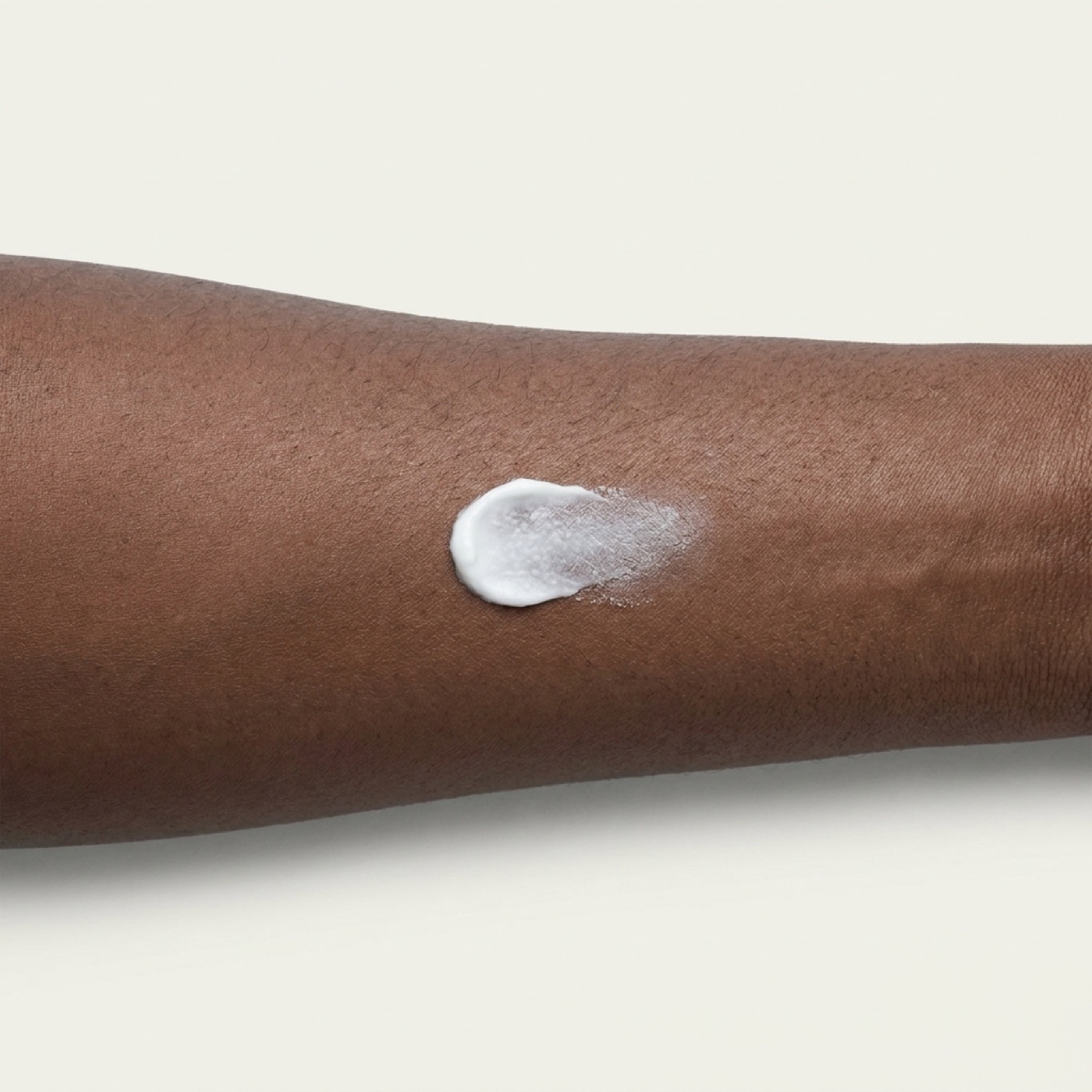 A swatch of white cream half rubbed into deep-brown inner-forearm skin, showing finish and white cast.
